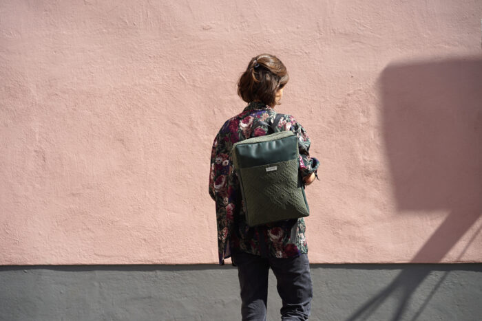 Dunkelgrüner Rucksack aus Leder mit Muster vor rosa Wand