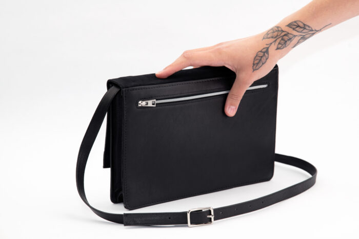 Rückseite einer schwarzen Handtasche mit Träger zum Verstellen und silbernem Reißverschluss