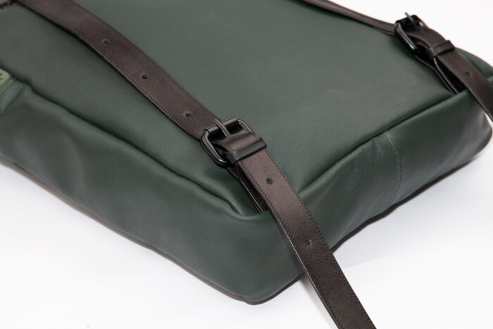 Detail eines grünen Rucksacks aus Leder mit schwarzen Schnallen und Trägern