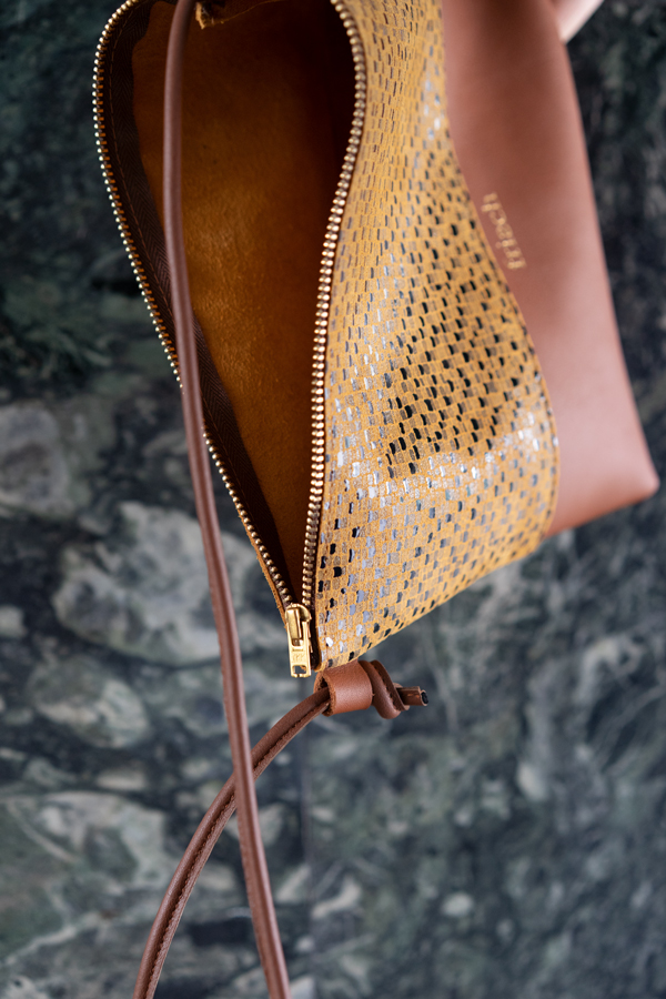 Close up einer Handtasche in senfgelb und braun vor Marmor Wand