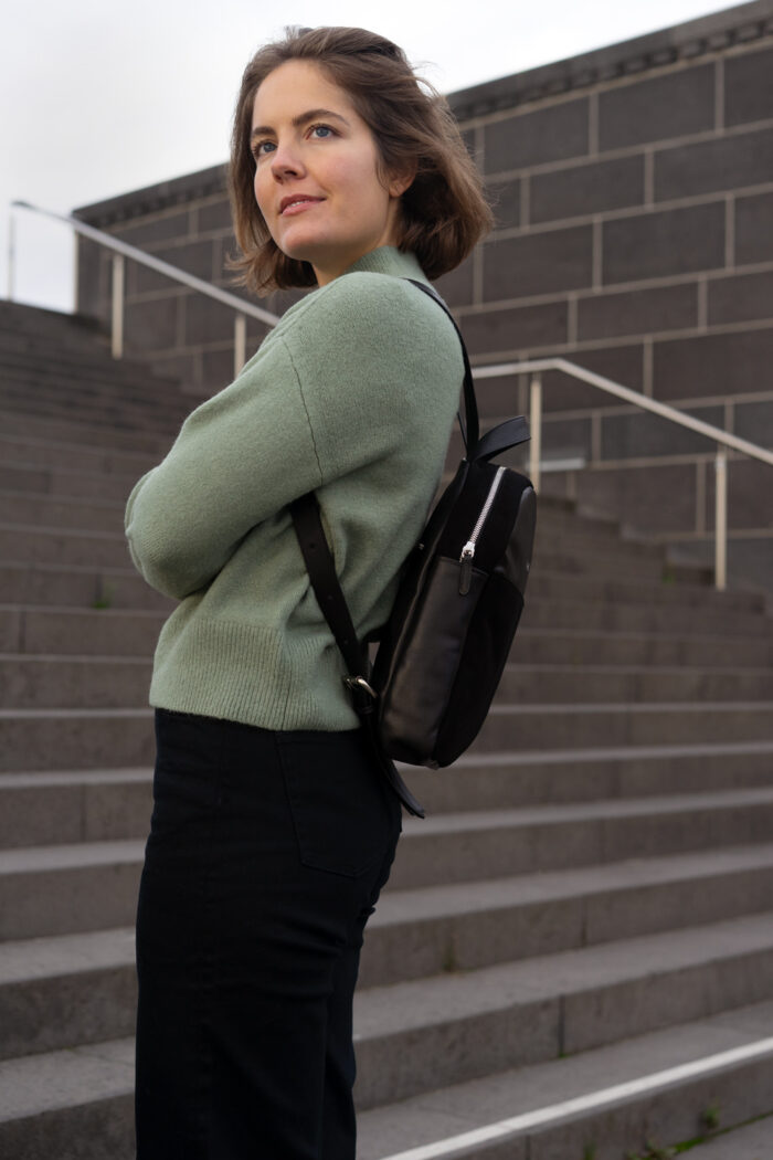 Model mit kleinem Rucksack in schwarz und grünem Pullover auf Treppe