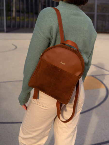 Model auf Sportplatz mit schickem Rucksack in braun und grünem Pullover