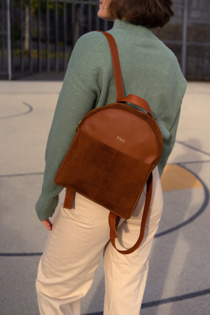 Model auf Sportplatz mit schickem Rucksack in braun und grünem Pullover