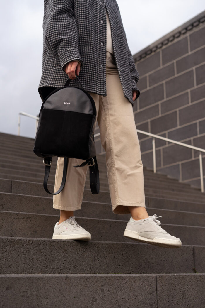 Model mit schwarzem Rucksack und Turnschuhen auf grauer Treppe