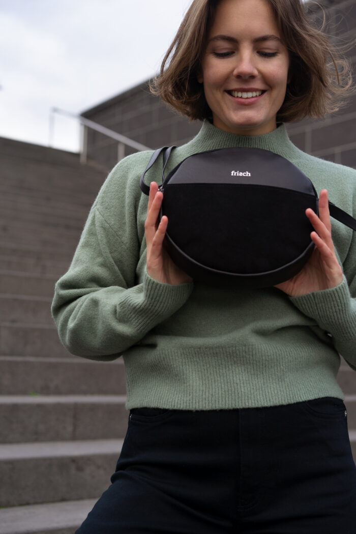 Model präsentiert schicke runde Handtasche in schwarz mit Logo