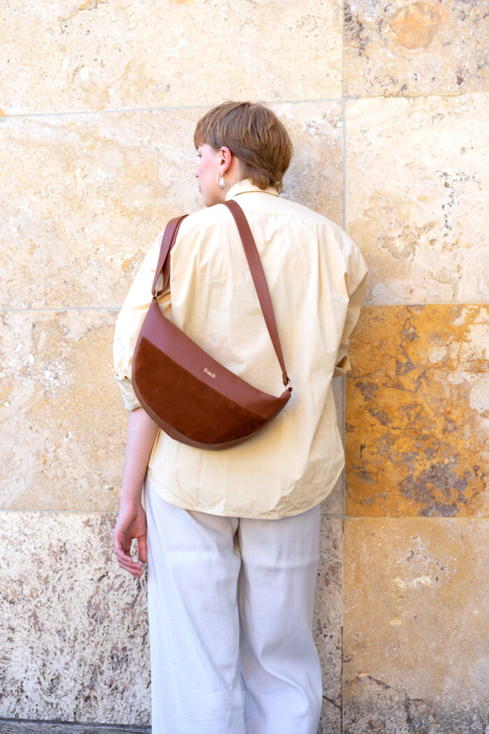 Model mit Handtasche über der Schulter aus braunem Leder vor marmorierter Steinwand