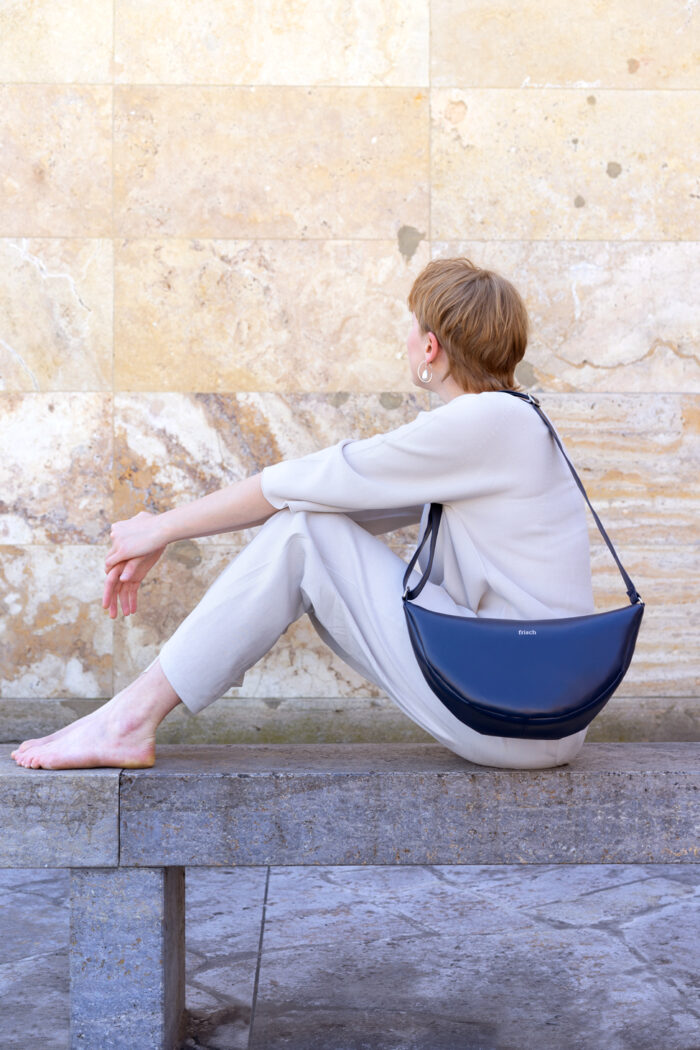 Model mit Handtasche aus dunkelblauem veganem Apfelleder vor marmorierter Steinwand