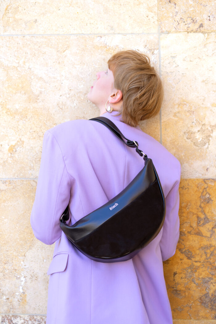 Model mit Lederhandtasche über der Schulter tragend mit fliederfarbenem Blazer